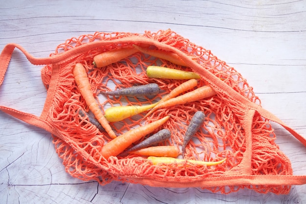 mixed colorful carrots and shopping bag on wooden background