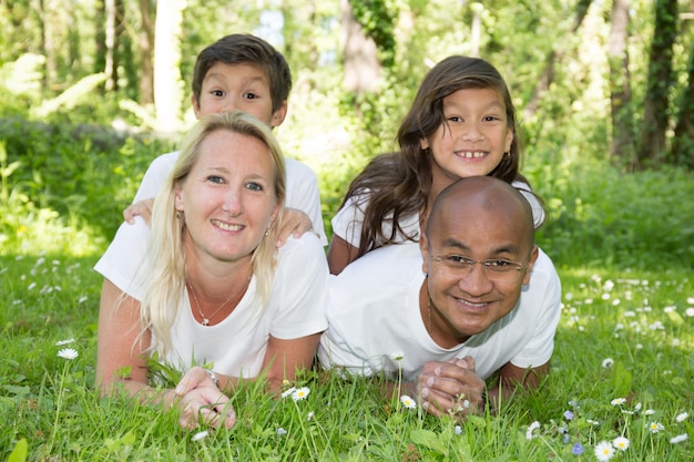 Mixed family of 4 with two children boy and girl lying in the grass during the summer