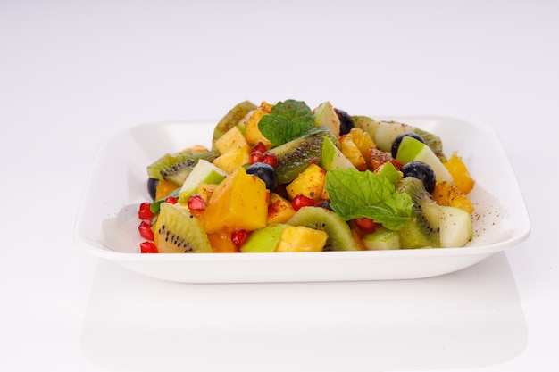 Mixed fruit salad arranged in a white tableware and garnished with mint leaf.