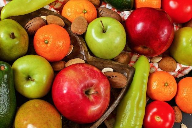 Mixed fruits and vegetables - red peppers, avocado, apples, pears, tangerines, pecan nuts, almonds and pumpkin seeds on wooden bowl, close up view from above.