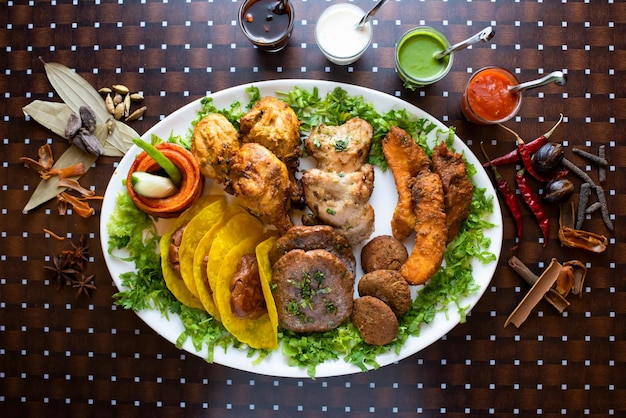 Mixed kabab platter with seekh kabab tikka boti raita mint sauce chutney and ketchup served in dish