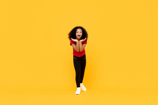 Mixed race Afro girl in surprised excited gesture with hands open isolated on yellow wall