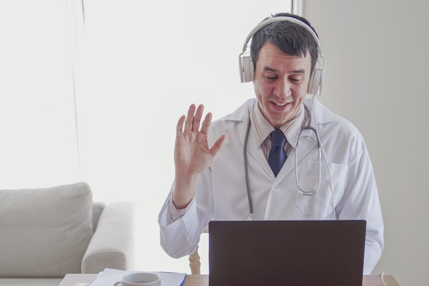 Foto medico in linea maschio medico asiatico di razza mista agitando la mano e lavorando a distanza