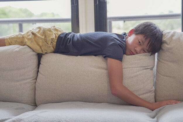 Mixed race Asian preteen boy feeling bored lying on sofa at home, social distancing, quarantine, isolation concept, autism awareness, mental health