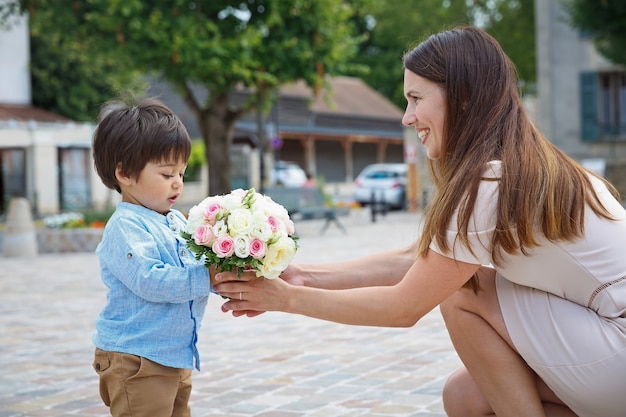 Mixed race boy little son congratulating his mom and giving her flower bouquet, they hugging and laughing together. Family holidays concept