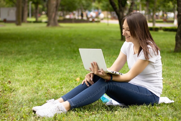 Studente di college di razza mista seduto sull'erba che lavora al computer portatile al campus