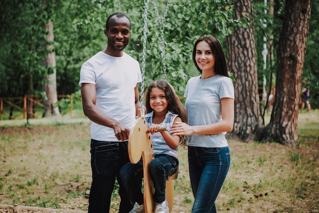 Mixed race family in park kid girl on horse swing