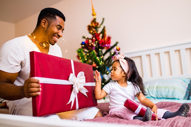 クリスマスの朝の寝室のベッドで休日を過ごす混血家族