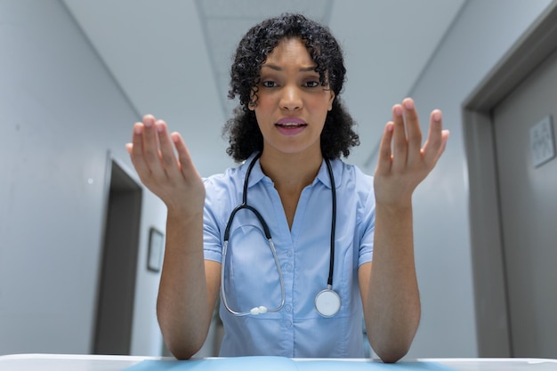 Mixed race female doctor at desk talking and gesturing during video call consultation