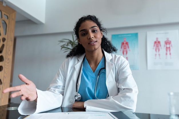 Mixed race female doctor at desk talking and gesturing during video call consultation