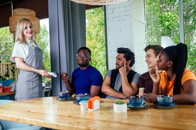 Mixed-race friends paying to waiter payment machine in cafe