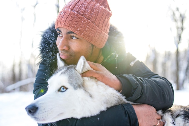 Mixed race man hug his dog husky in winter forest park