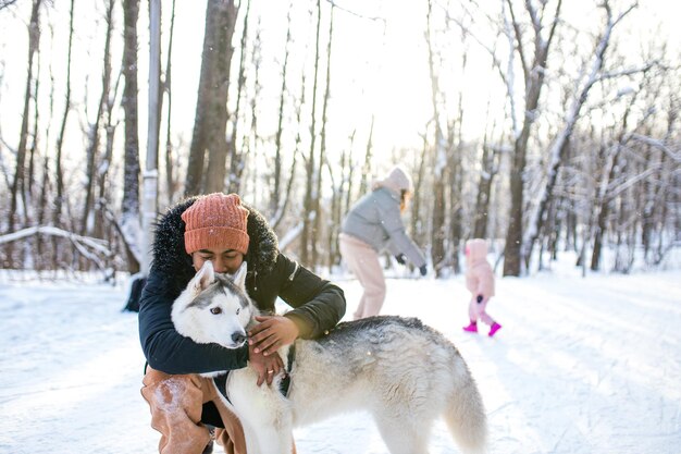 Mixed race man hug his dog husky in winter forest park