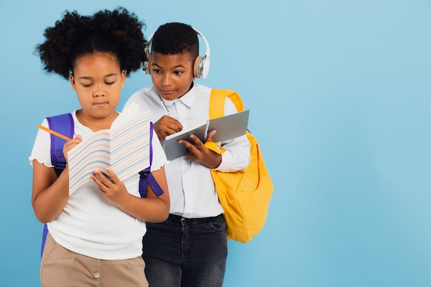 Mixed race schoolboy handing off homework to african american schoolgirl in school classroom on blue background back to school concept