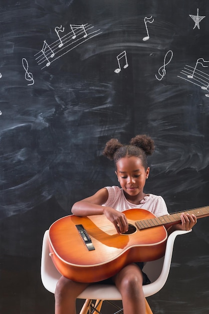 Mixed race schoolgirl playing the guitar while in music\
school