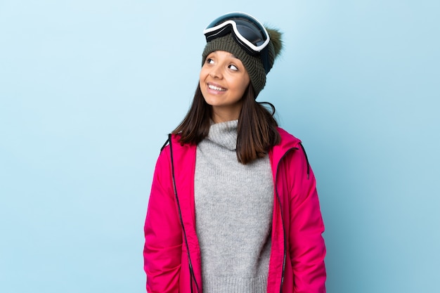 Foto ragazza dello sciatore della corsa mista con i vetri di snowboard sopra il blu isolato che pensa un'idea mentre guardando su