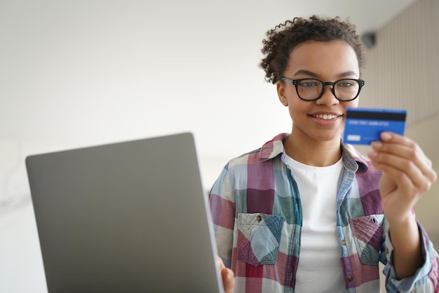 Mixed race teen girl holds credit card using online banking services at laptop at home E commerce