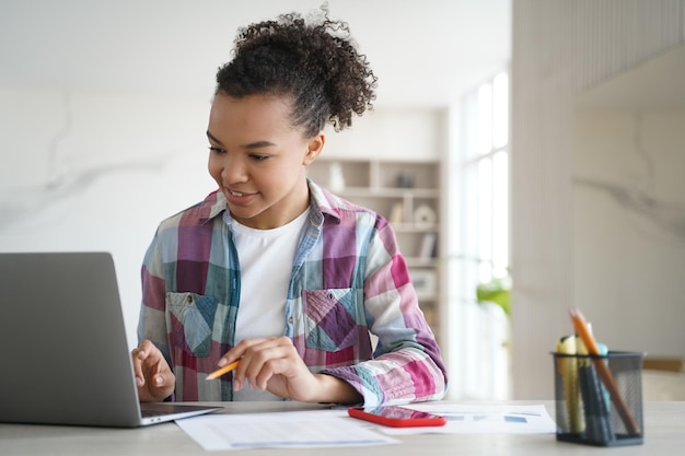 Mixed race teen girl student looking at laptop screen learning online at home Distance education