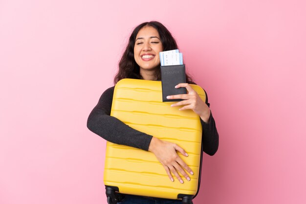 Mixed race woman over isolated pink wall in vacation with suitcase and passport