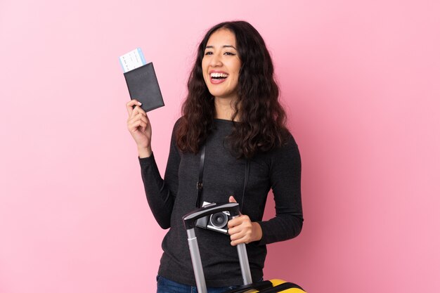 Mixed race woman over isolated pink wall in vacation with suitcase and passport