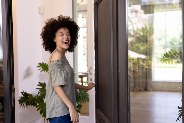 Mixed race woman returning home, walking through the front doors, holding a door handle, looking at the camera and smiling