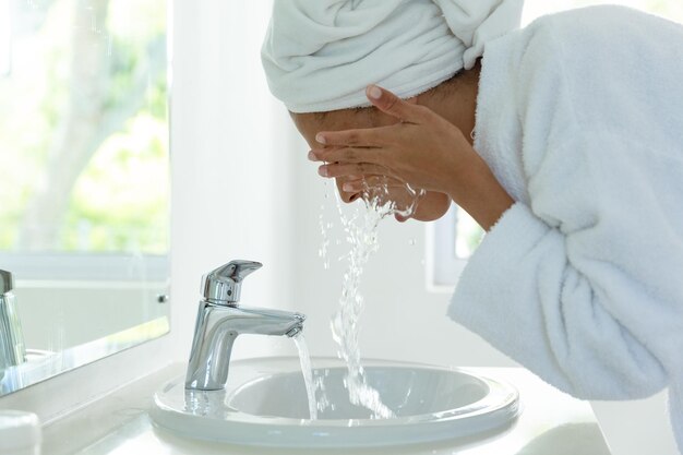 Mixed race woman wearing bathrobe and washing her face in bathroom