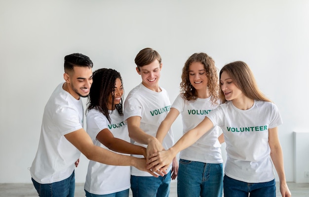 Mixed race young volunteers joining hands together and smiling
ready for work in charity organization center