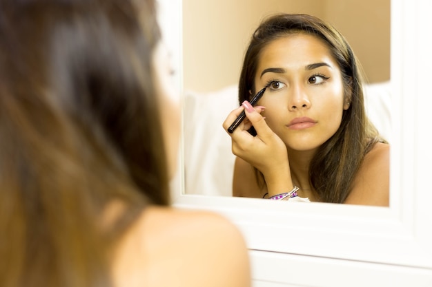 Mixed race young woman with brush eye liner on looking in the mirror