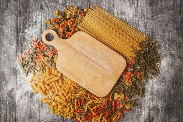 Mixed raw pasta on a black wooden background, strewn with flour.