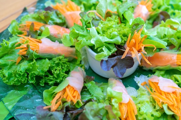 Mixed salad and vegetable roll are arranged on glass dish with sauce beside