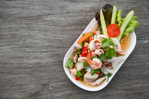 Mixed salad with shrimp squid pork sausage with fresh vegetable cucumber celery leaf on plate on wooden table Thai food salad