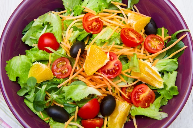 Mixed salad with tomatoes in purple bowl on wood table