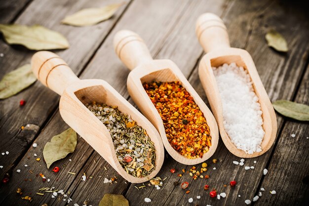 Mixed spices for fish and chicken cooking and salt in wooden scoops, bay leaves and pepper corns on old vintage table