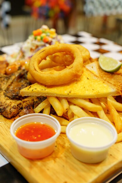 Mixed steak and french fries with dipping sauce on a wooden chopping board