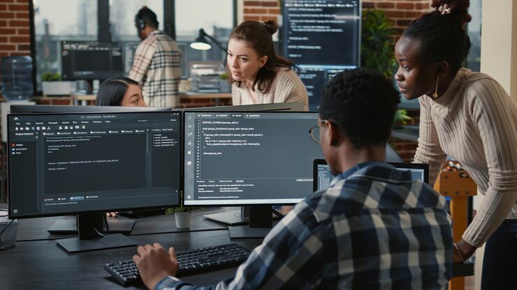Photo mixed team of artificial intelligence cloud programers talking about programming in front of multiple screens compiling code. programmers doing teamwork looking at machine learning algorithms.
