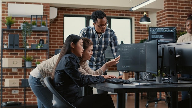 Mixed team of software engineers brainstorming ideas for new cloud computing user interface looking at running code on computer screens. Programmers collaborating on group project compiling algorithm.