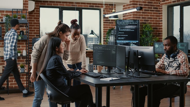 Photo mixed team of software engineers brainstorming ideas for new code library in front of computer screens compiling algorithms. diverse app developers collaborating on group project in it agency office.