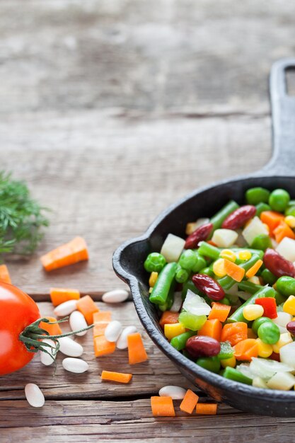 Mixed vegetable meal in old iron frying pan closeup and ingredients on wooden rustic table