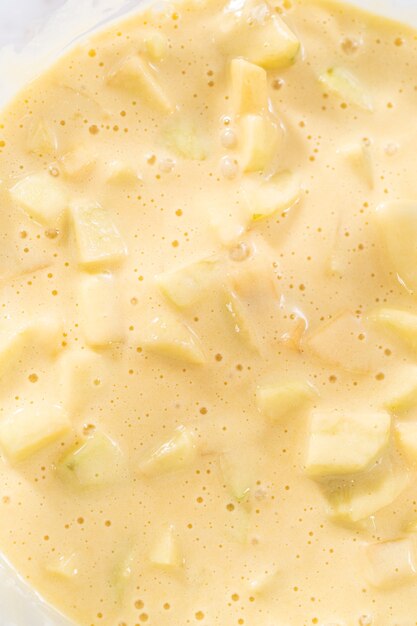 Mixing ingredients in a large glass mixing bowl to bake apple sharlotka muffin.