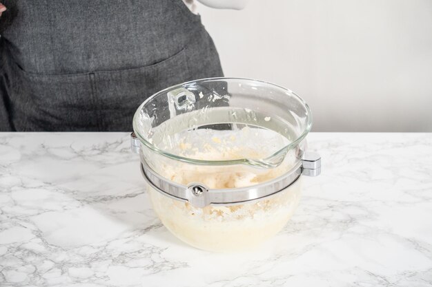 Mixing ingredients in a large glass mixing bowl of kitchen mixer to make eggnog buttercream frosting.