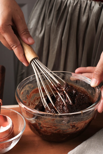 사진 큰 볼에 녹인 초콜릿과 코코아 가루를 섞어 발롱 털을 사용하여 나무 테이블에 맛있는 홈메이드 브라우니 케이크를 만들기 위한 반죽/믹스/배터 만들기