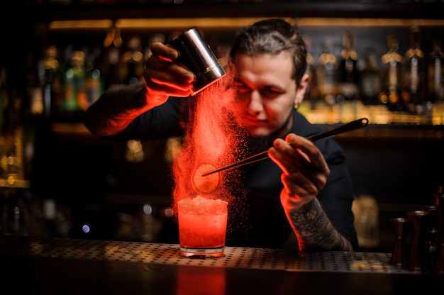 Mixologist kruidenpoeder toevoegen aan een cocktailglas met schijfje citroen