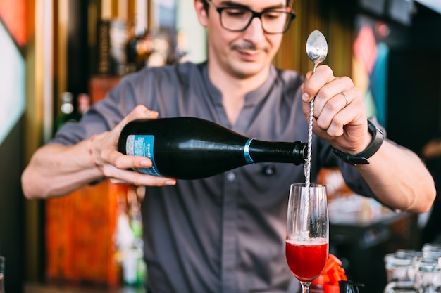 ミクソロジストがグラスに長いスプーンでワインを注ぐことにより、赤のイタリアのソーダカクテルを作ります。