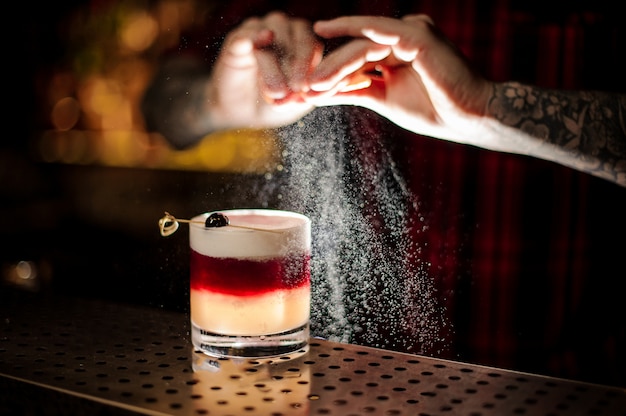 Mixologist sprinkling orange juice into a glass of sweet flaky cocktail