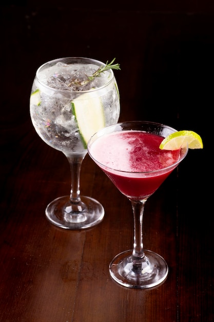 Mixology two cocktail glasses with martini berries gin cucumber rosemary ice on wooden table