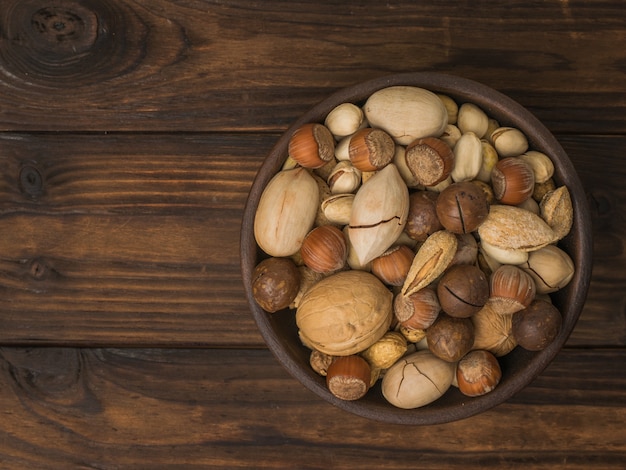 A mixture of a large number of different nuts in a clay cup on a wooden table. Vegetarian food.