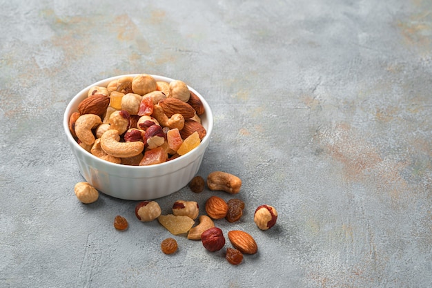 A mixture of nuts and dried fruits in a white cup on a gray wall with space to copy. Side view, horizontal.