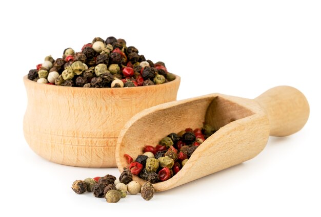 A mixture of peppers in a wooden plate and a spoon close-up on a white