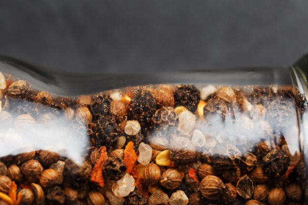 A mixture of seasonings spices and herbs in a glass mill on a black background