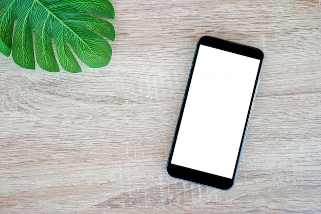 mobiele smartphone met leeg scherm en monstera bladeren op houten tafel